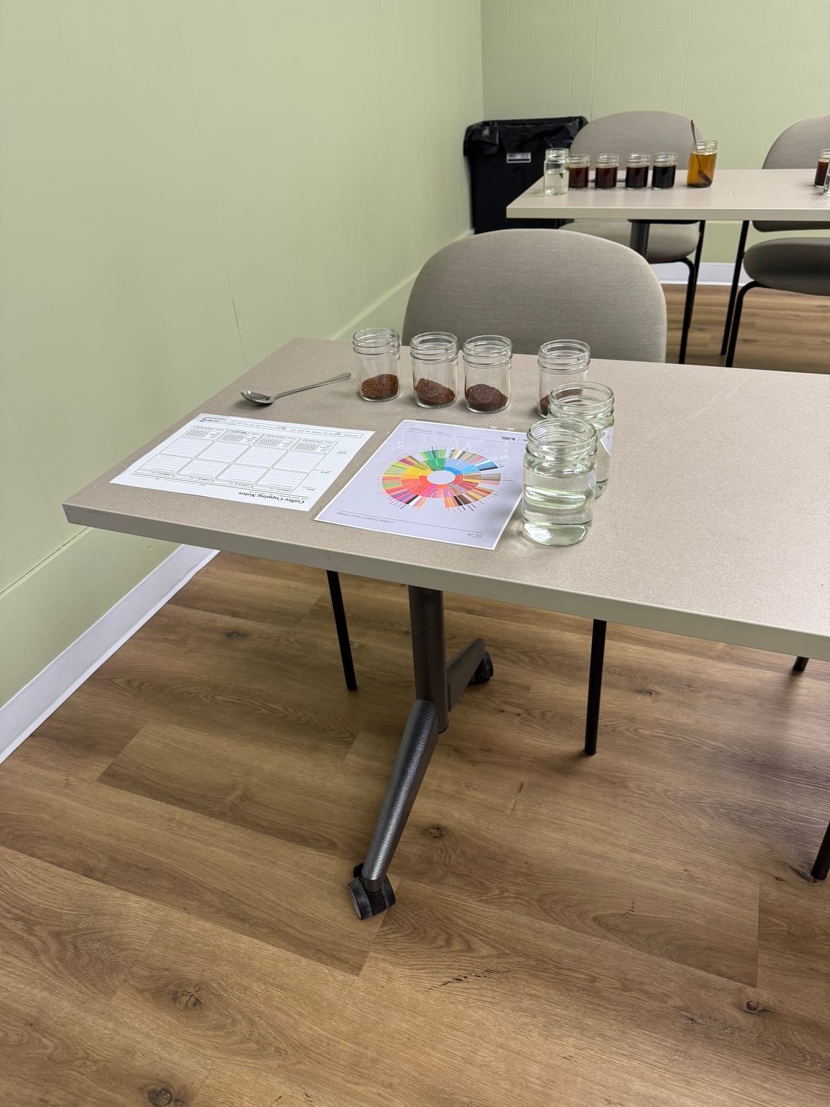 A coffee cupping table set with tasting glasses and an SCA flavor wheel
